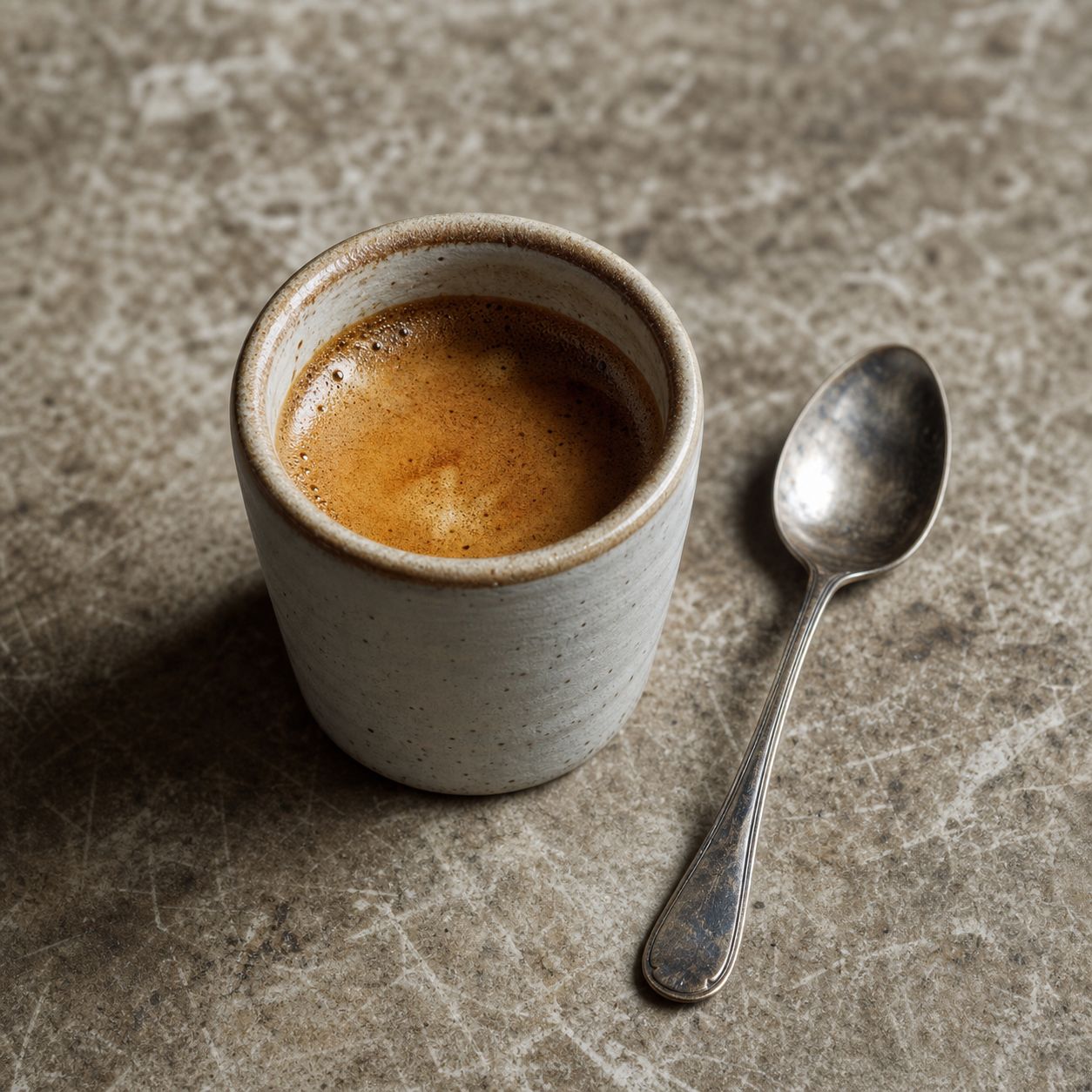Café expresso em copo de cerâmica com uma colher gasta ao lado.