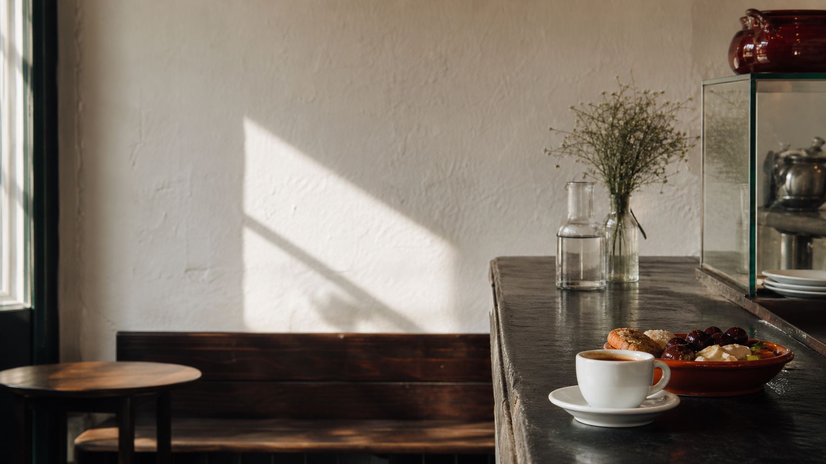 Chávena de café e prato de petiscos num balcão iluminado pelo sol.